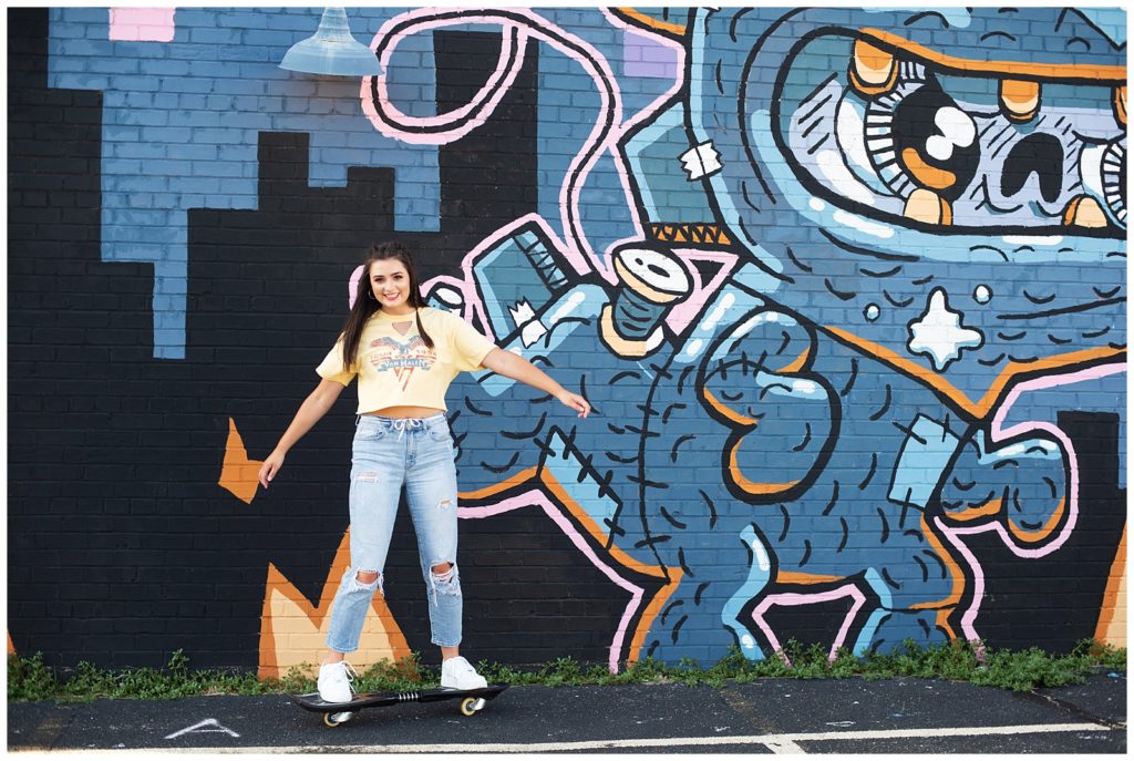 senior girl skateboarding in front of mural graphic tee