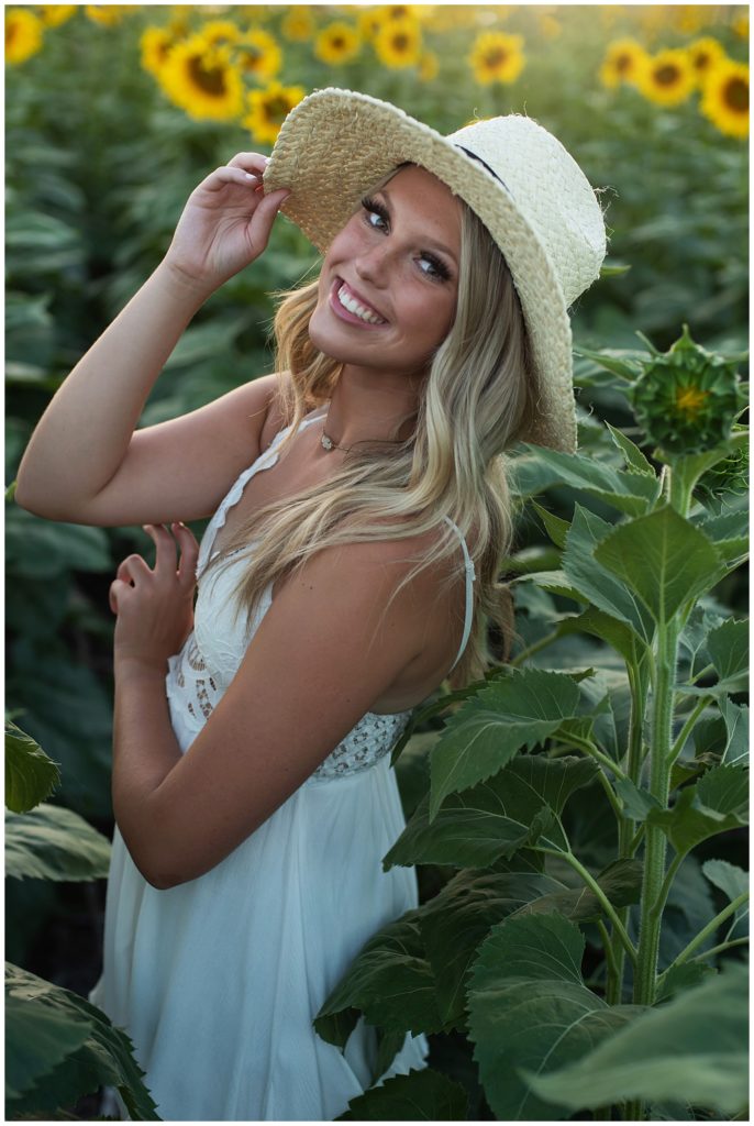 senior girl white dress and hat laughing sunflower field