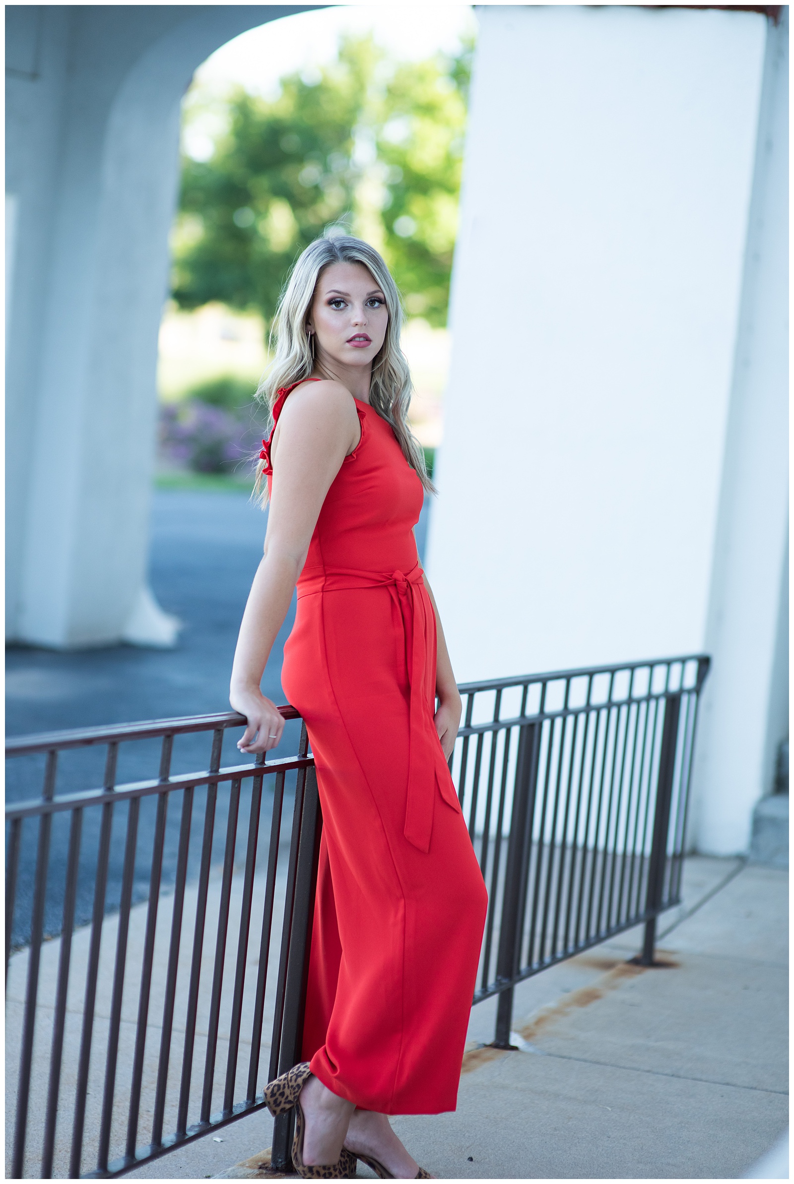 high school senior in red jumpsuit leaning on black iron fence senior pictures