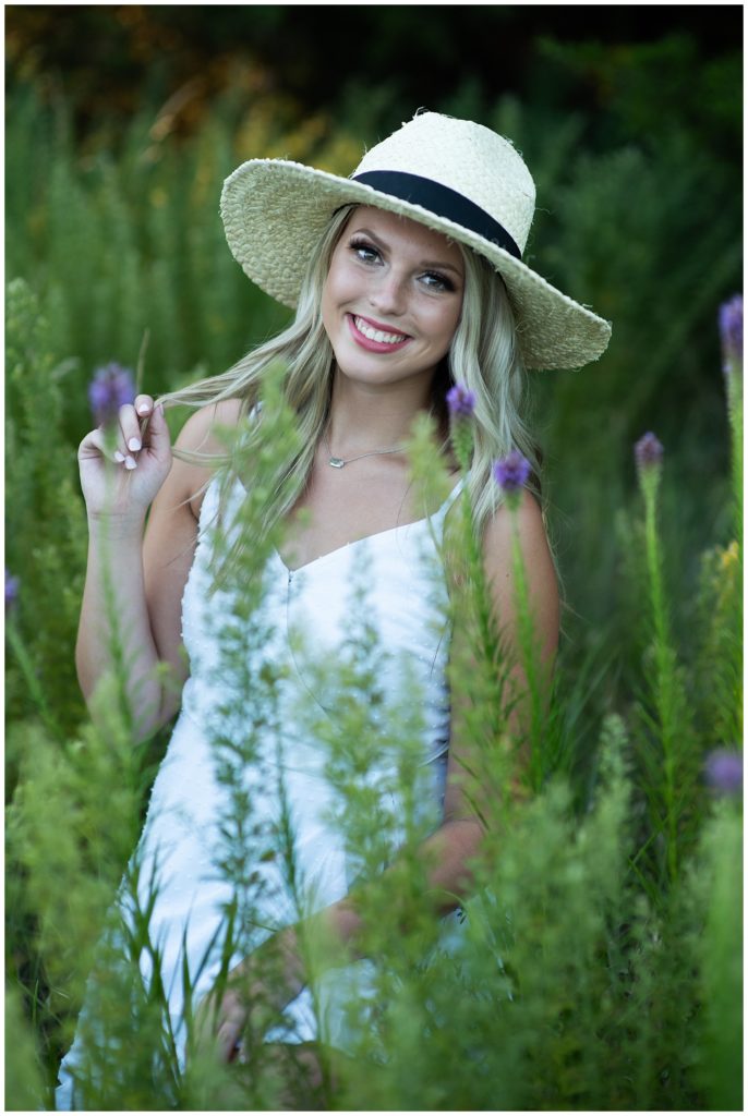 High School Senior Portraits in flower field.  Girl in white dress and hat.