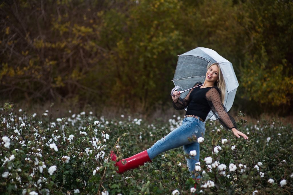 High School senior pictures Wichita, KS girl prancing through cotton field with. red boots and umbrella