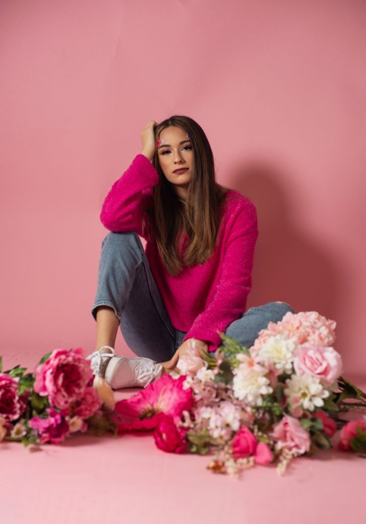 girl in pink sweater sitting against pink backdrop with flowers