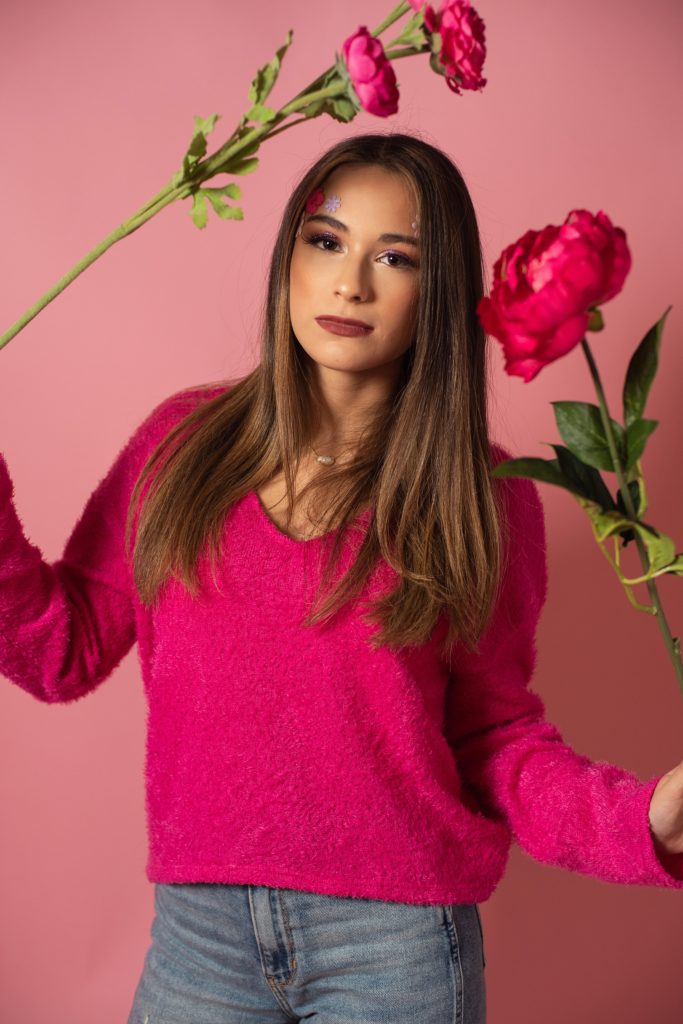 high school senior girl holding flowers pink background