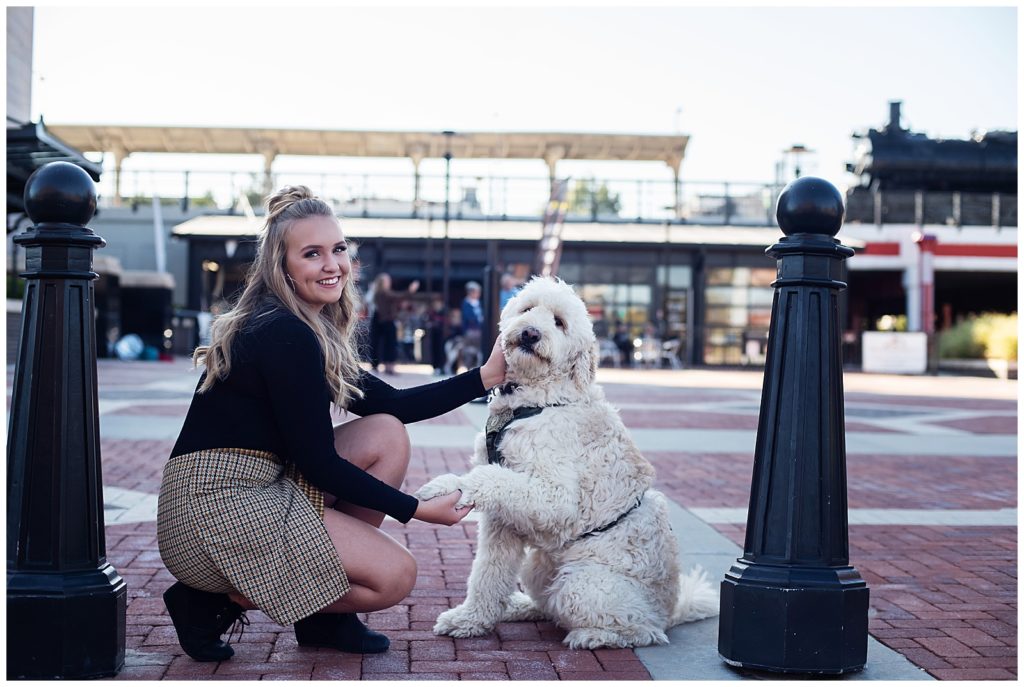 high school senior girl posing with heer golden doodle dog in an urban setting