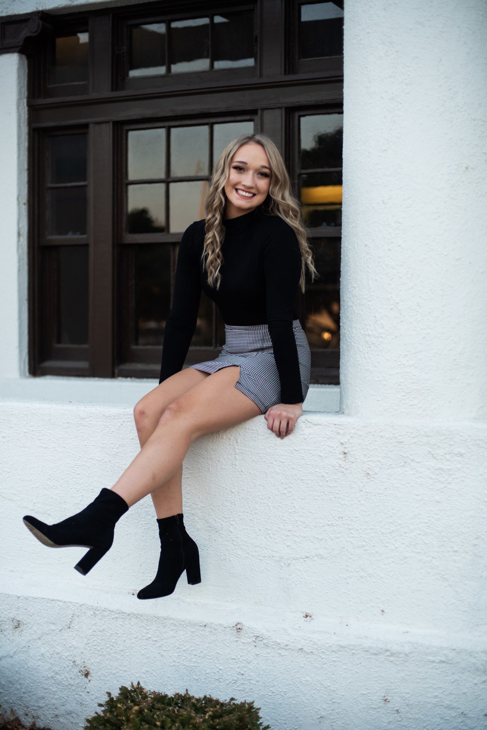 high school senior in black sweater and skirt with black booties sitting in window well senior pictures Kim Stiffler Photography