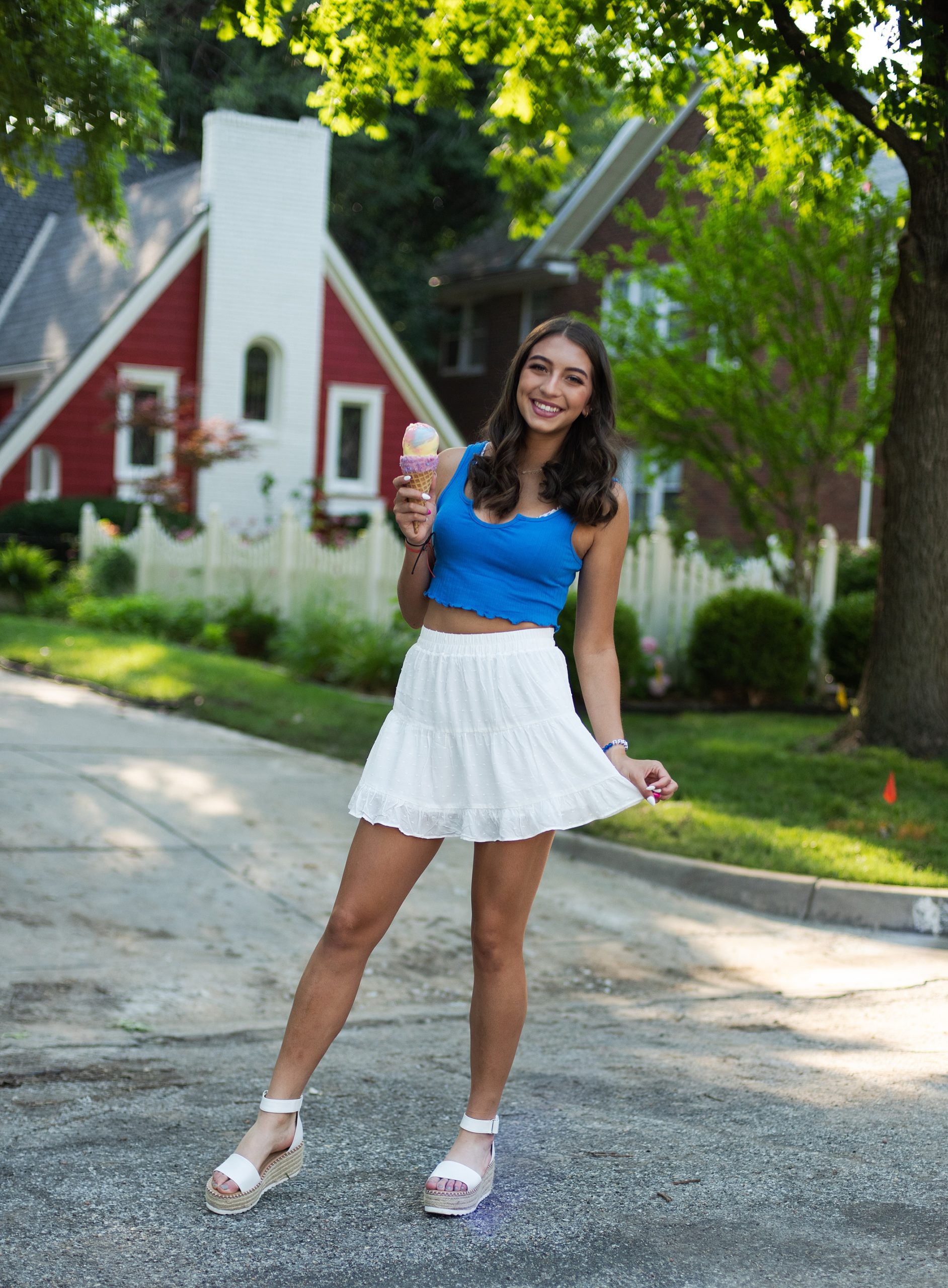 high school senior in front of red house in blue top and white skirt holding ice cream cone senior pictures