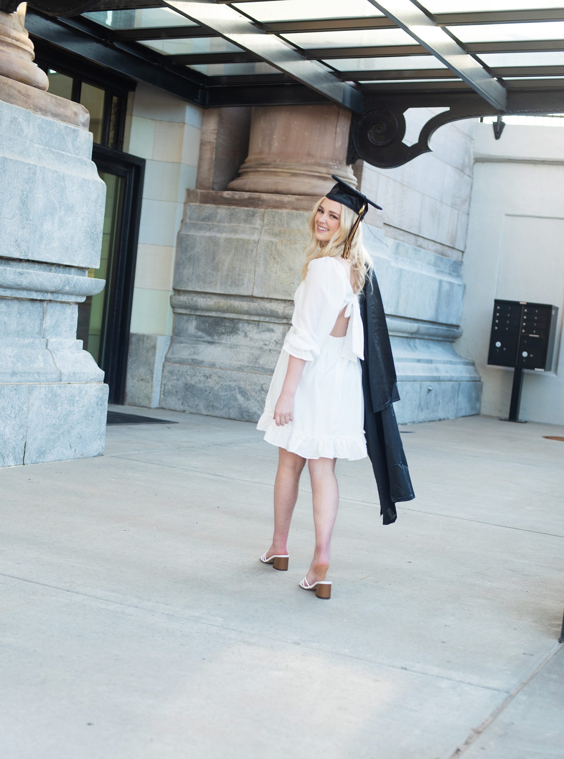 high school senior in white dress, grad hat, and carrying gown over shoulder senior pictures