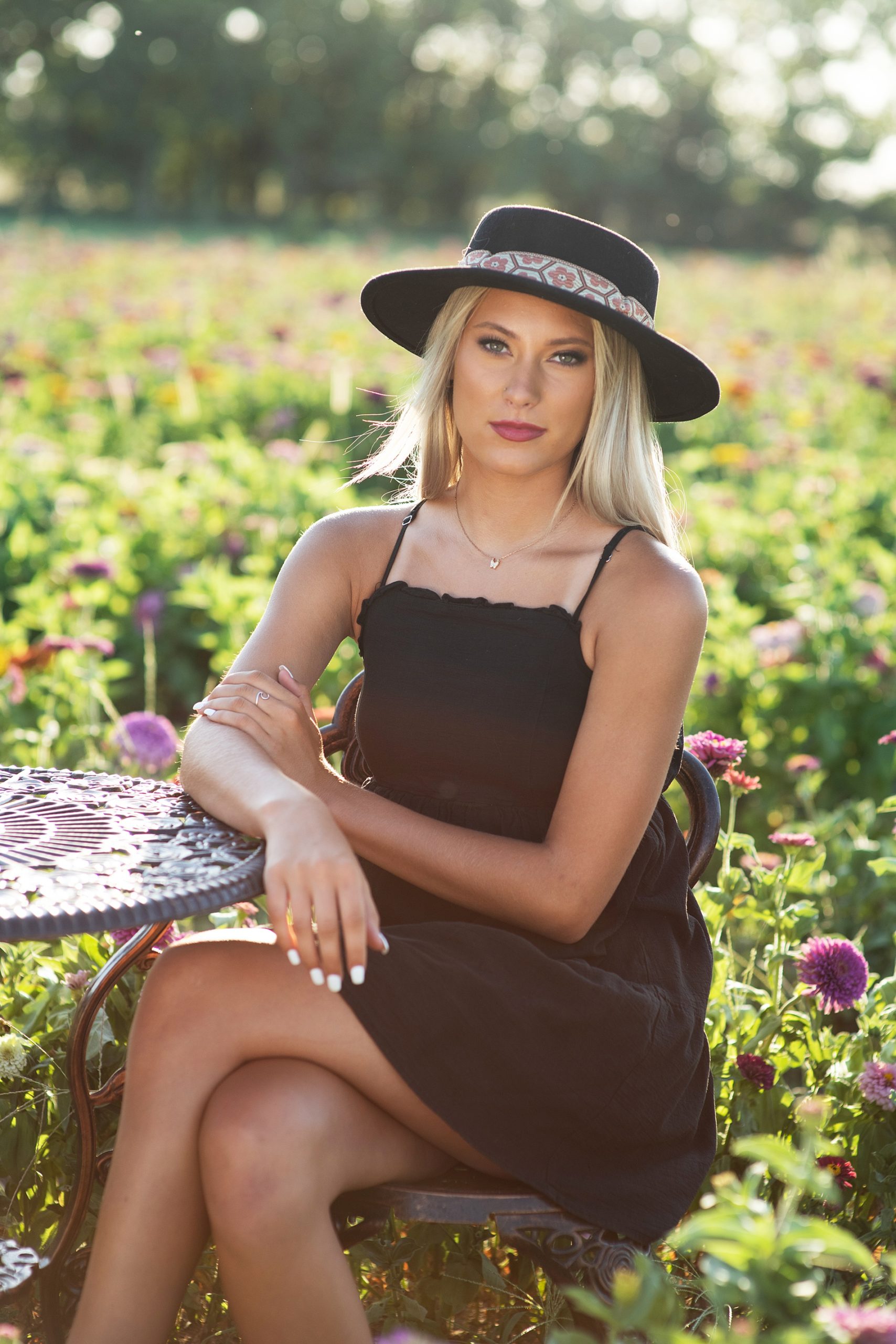 high school senior girl in black dress and hat in field of zinnias senior pictures