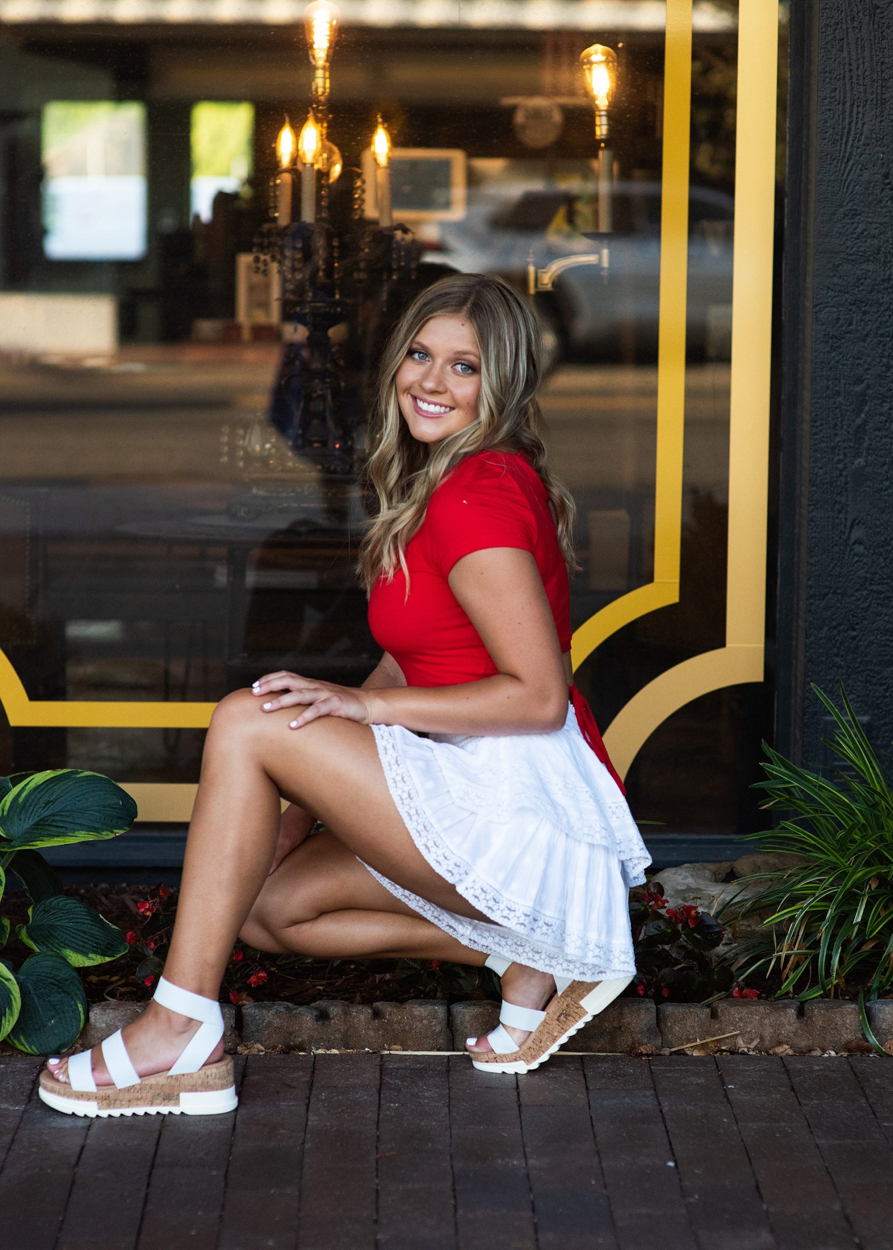 high school senior in red top and white skirt in front of storefront Kim Stiffler Photography