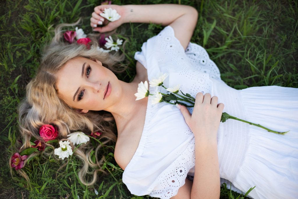 high school senior girl in white dress lying in field flowers in her hair senior pictures