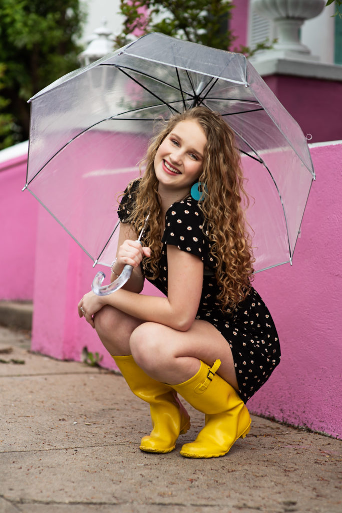 high school senior in yellow boots with clear umbrella in front of pink house Kim Stiffler Photography