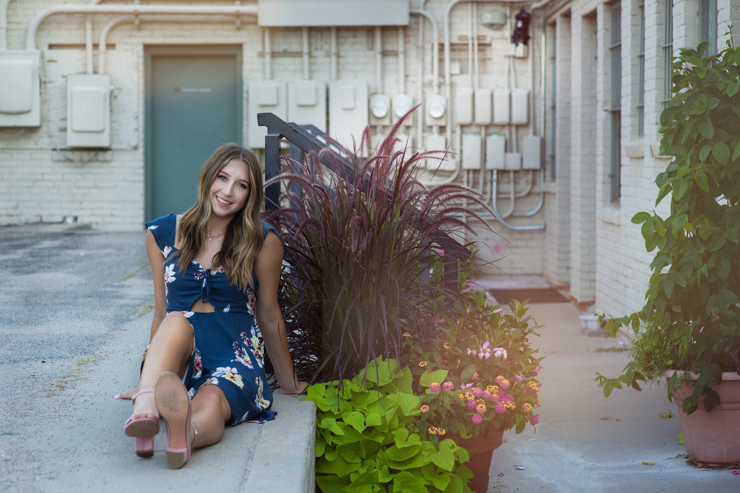 high school senior in blue dress sitting in front of building and plants Kim Stiffler Photography