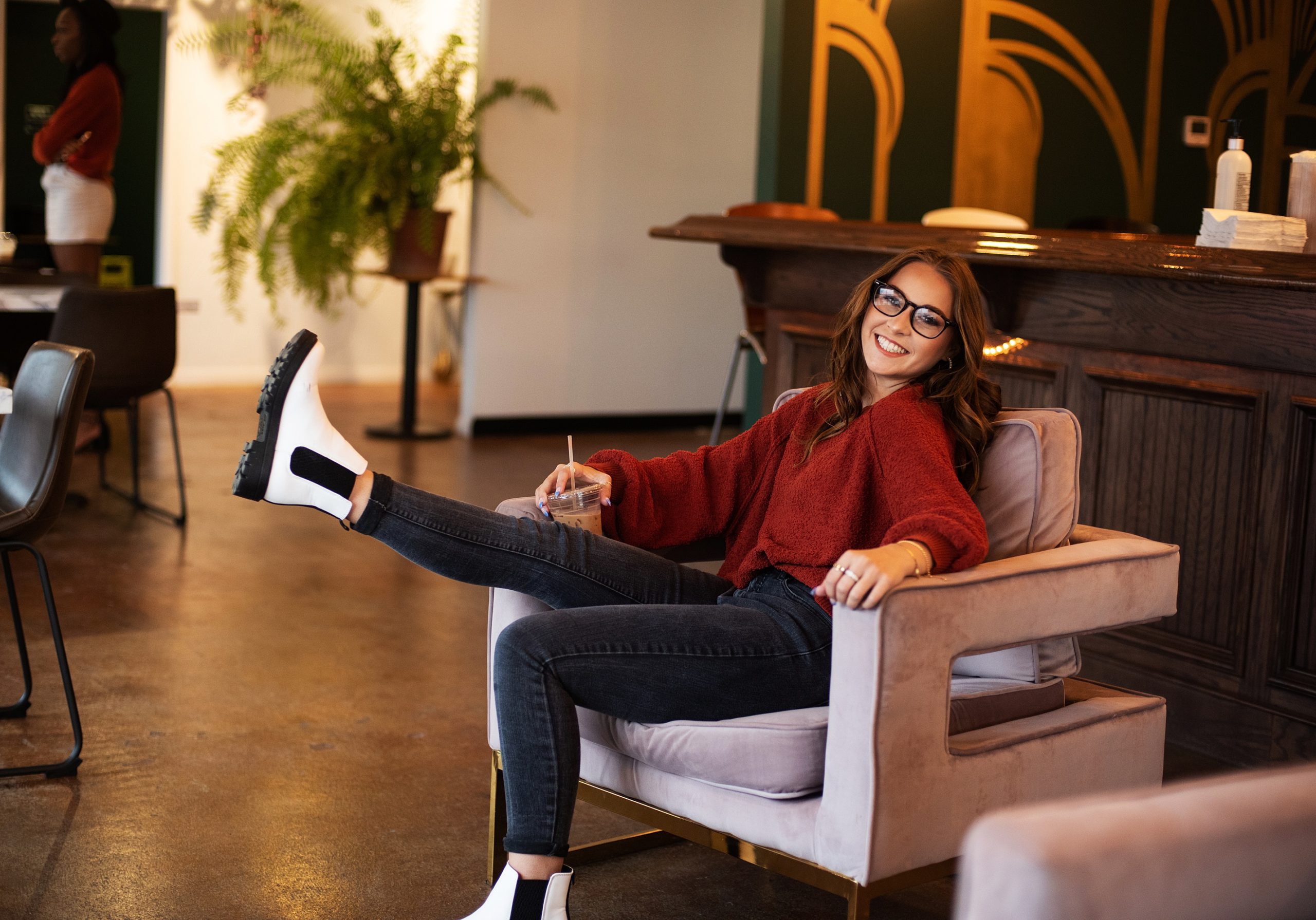 high school senior girl in pink chair in coffee shoop kicking out leg and smiling senior pictures