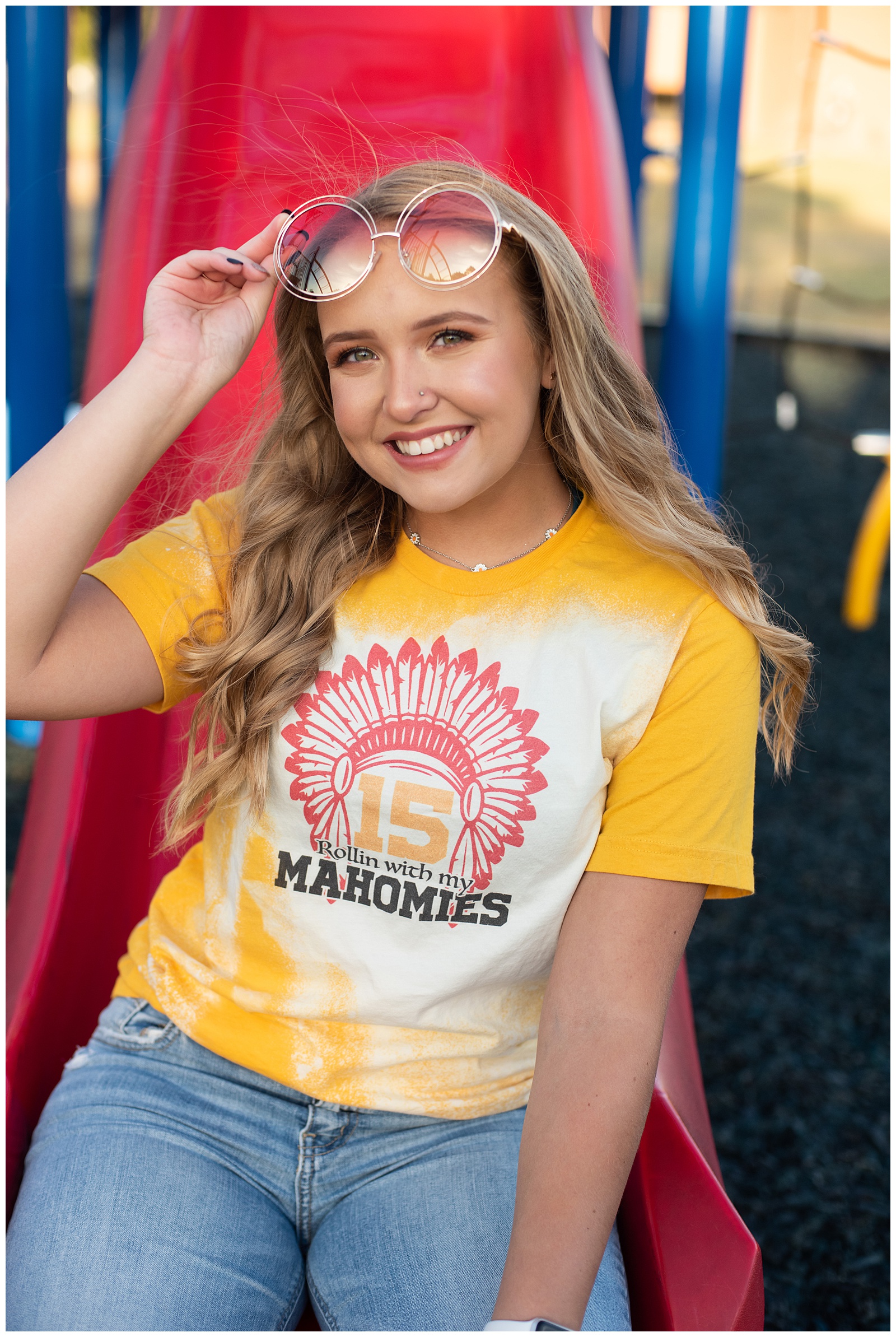high school senior girl in yellow and red KC Chiefs shirt on playground senior pics
