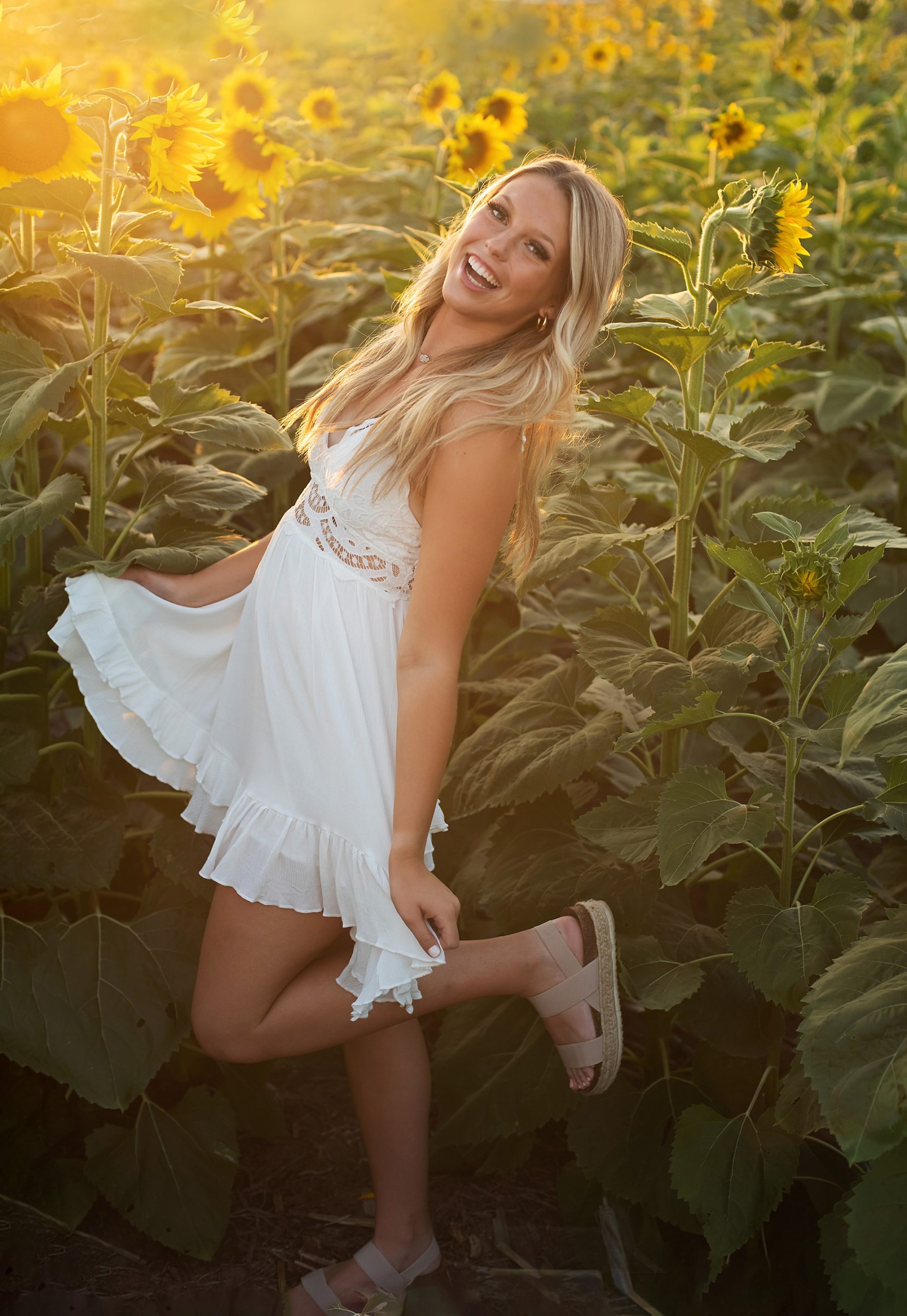 high school senior girl in white dress twirling laughing in sunflower field senior pictures