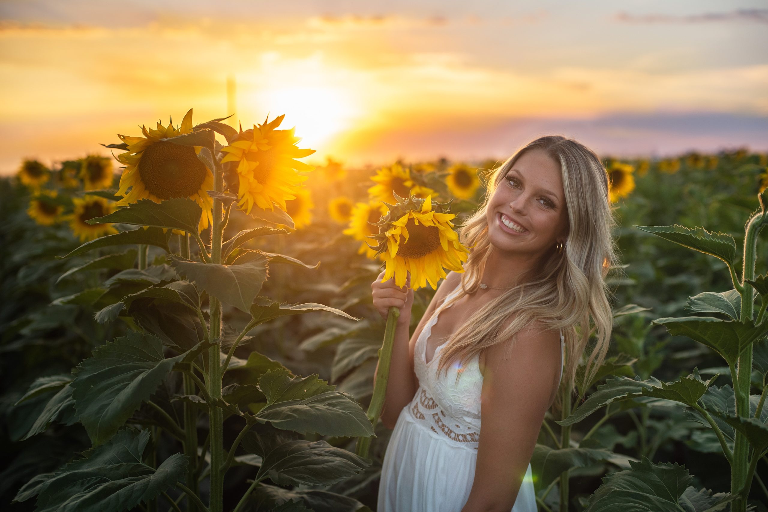 high. school senior girl in sunflower field with sun going down behind her senior pictures