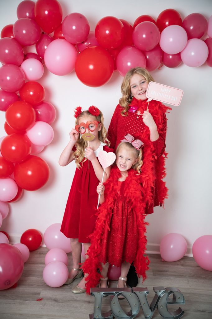 Valentine Mini Session three girls in red dresses with balloons in background.