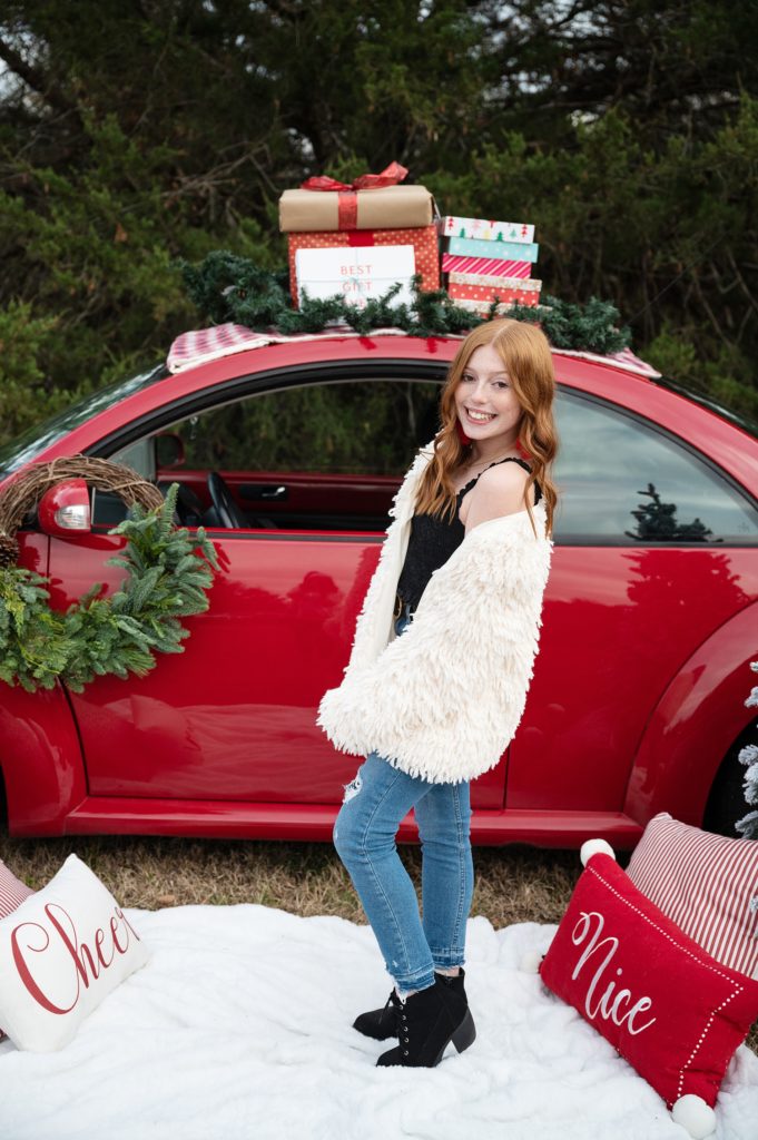 Red VW bug decorated for Christmas teen in white coat taking photos