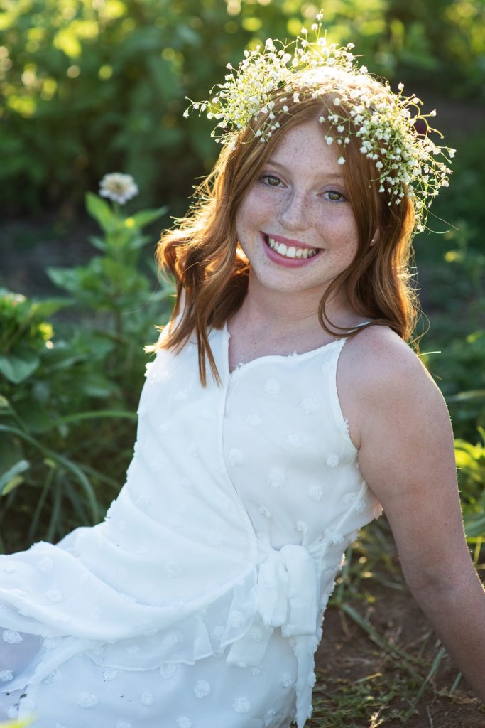 girl in white dress and flower crown in field of zinnias