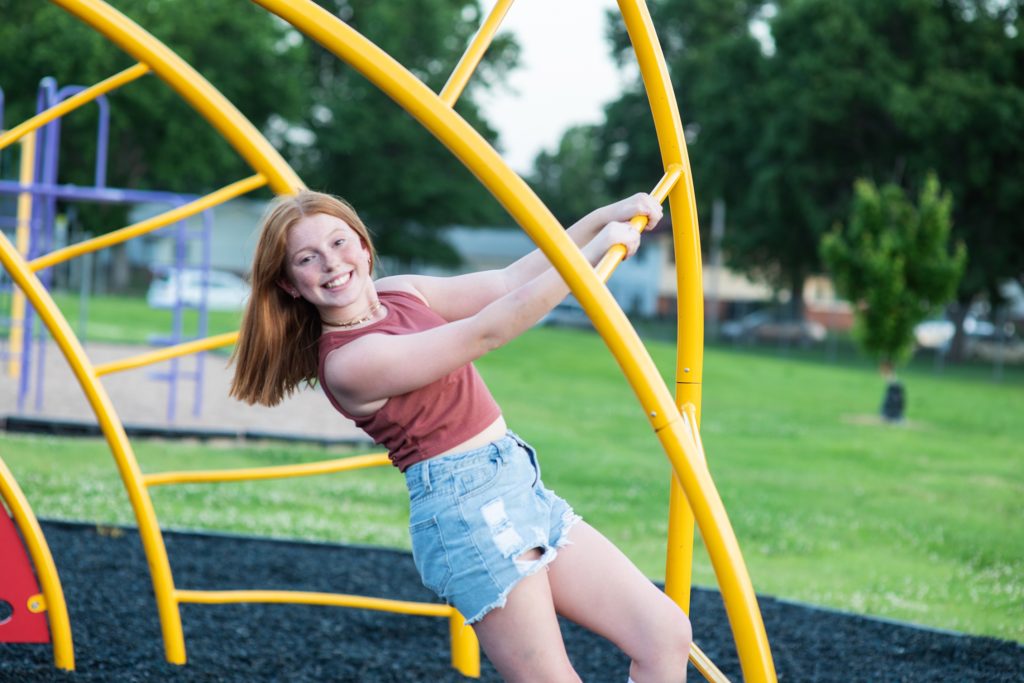 girl in maroon top and jean shorts on playground equipment