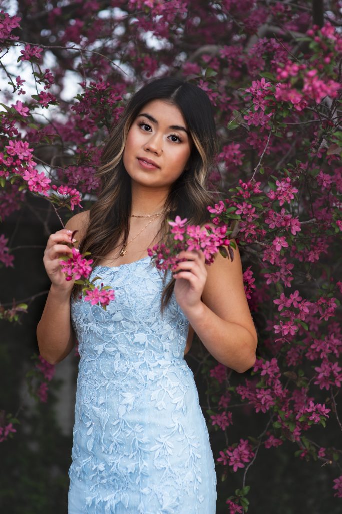 high school senior girl in blue prom dress in purple flowering tree for senior pictures