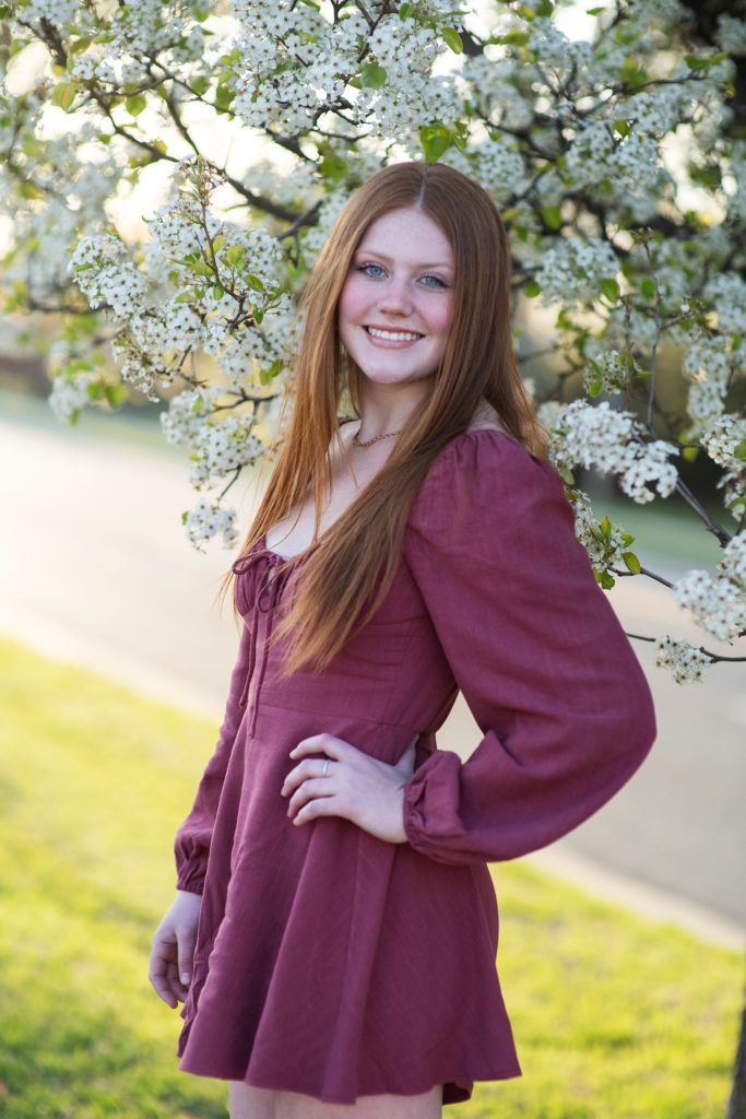 high school senior girl in magenta dress smiling in front of a blooming pear tree