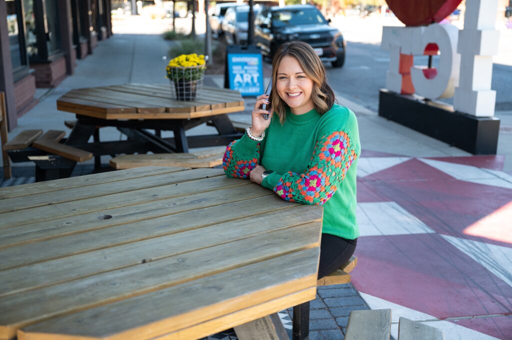 woman in green sweater talking on cell phone at outdoor table