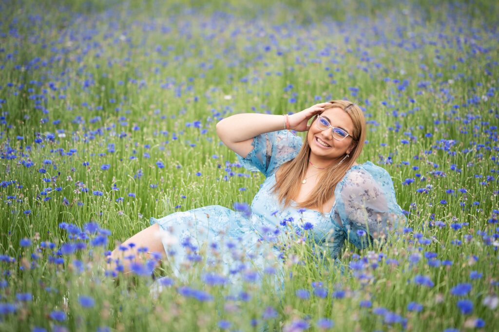 high school senior girl with brown hair lying in a field of blue flowers fo senior pictures